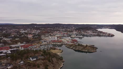 aerial approaching grimstad city above sea with soft reflections during morning - wooden white houses and marina in southern norway archipelago