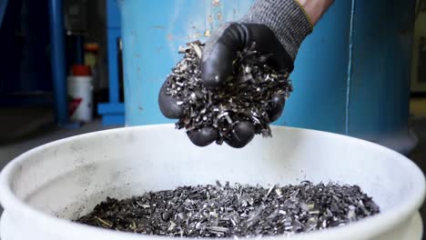 a gloved hand grabs metal turnings from a bucket in slow motion