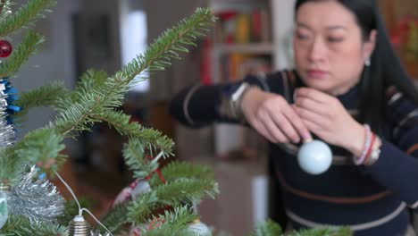 After-the-holidays,-an-Asian-woman-is-removing-ornaments-from-the-Christmas-tree