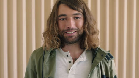 portrait of relaxed friendly young caucasian man with long hair smiling happy looking at camera wooden background