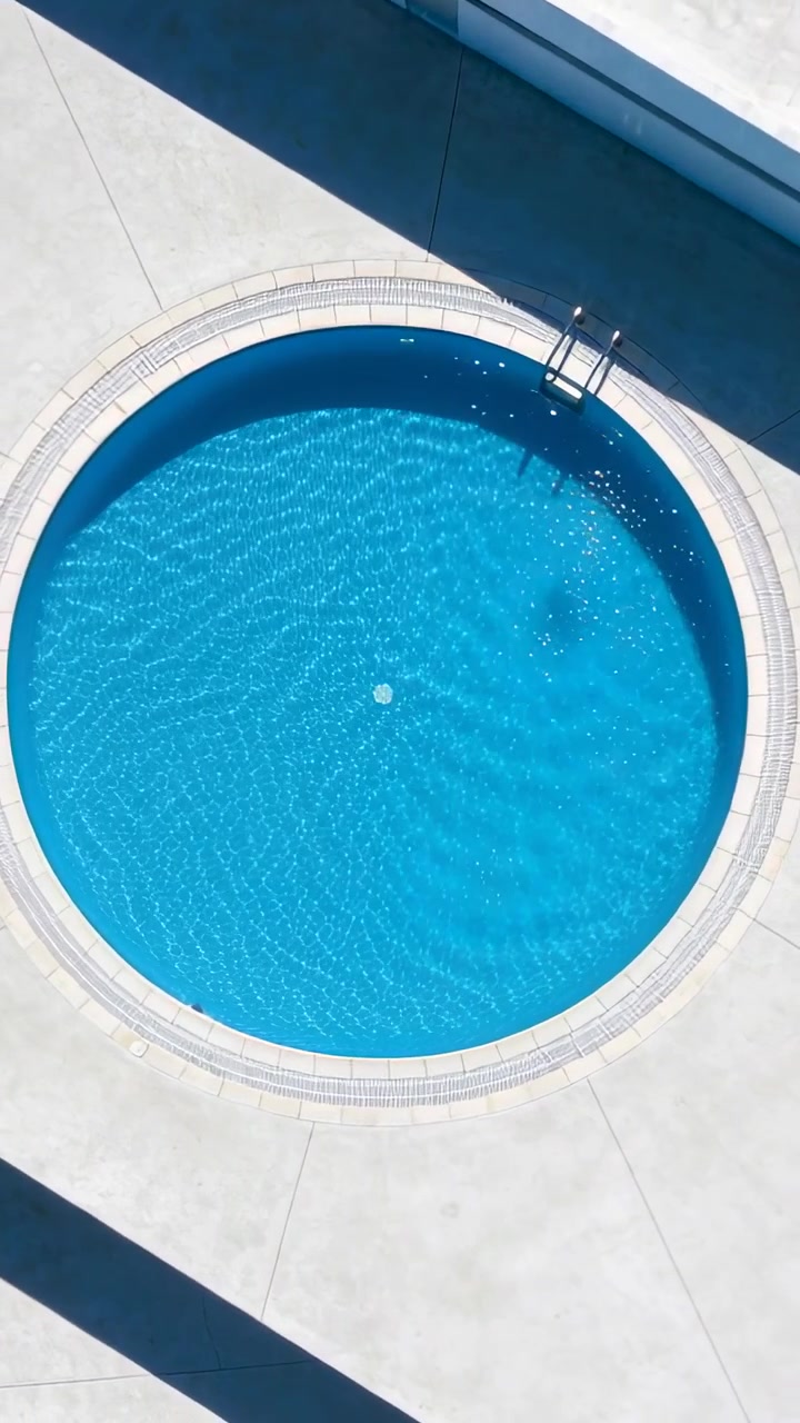 Vertical video: Rippling round pool water flowing from jet drifting float by ladder at pool deck
