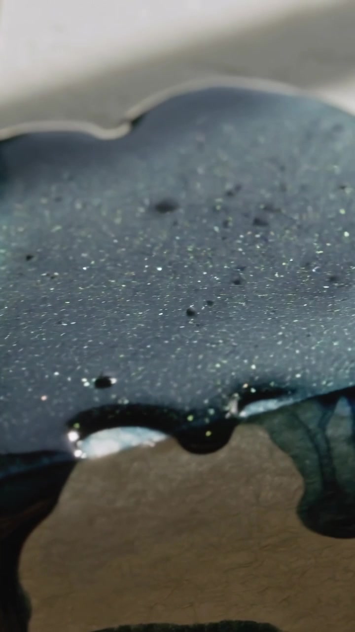 Vertical video: Lowering rod dropping teal resin, coating jigsaw on light table, yellow blob nearby