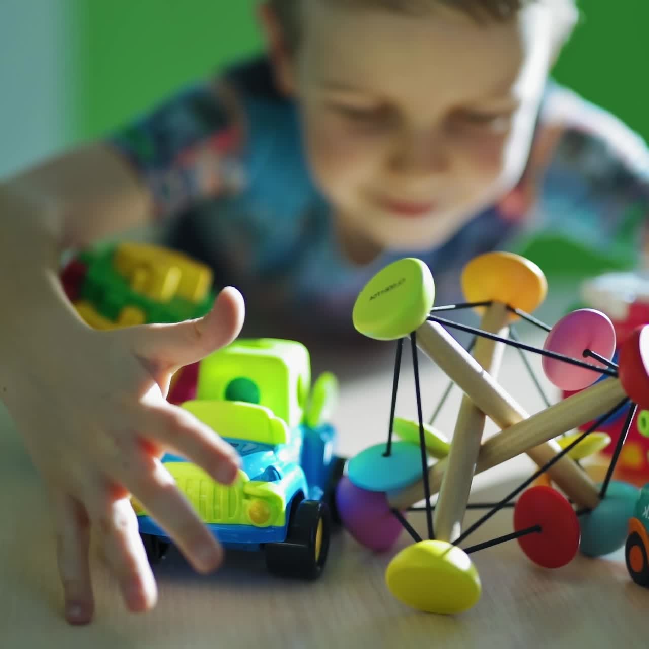 Colorful toys on the table. Little boy captures toys together in the room. Satisfied child with many toys. Close-up. Slow motion.