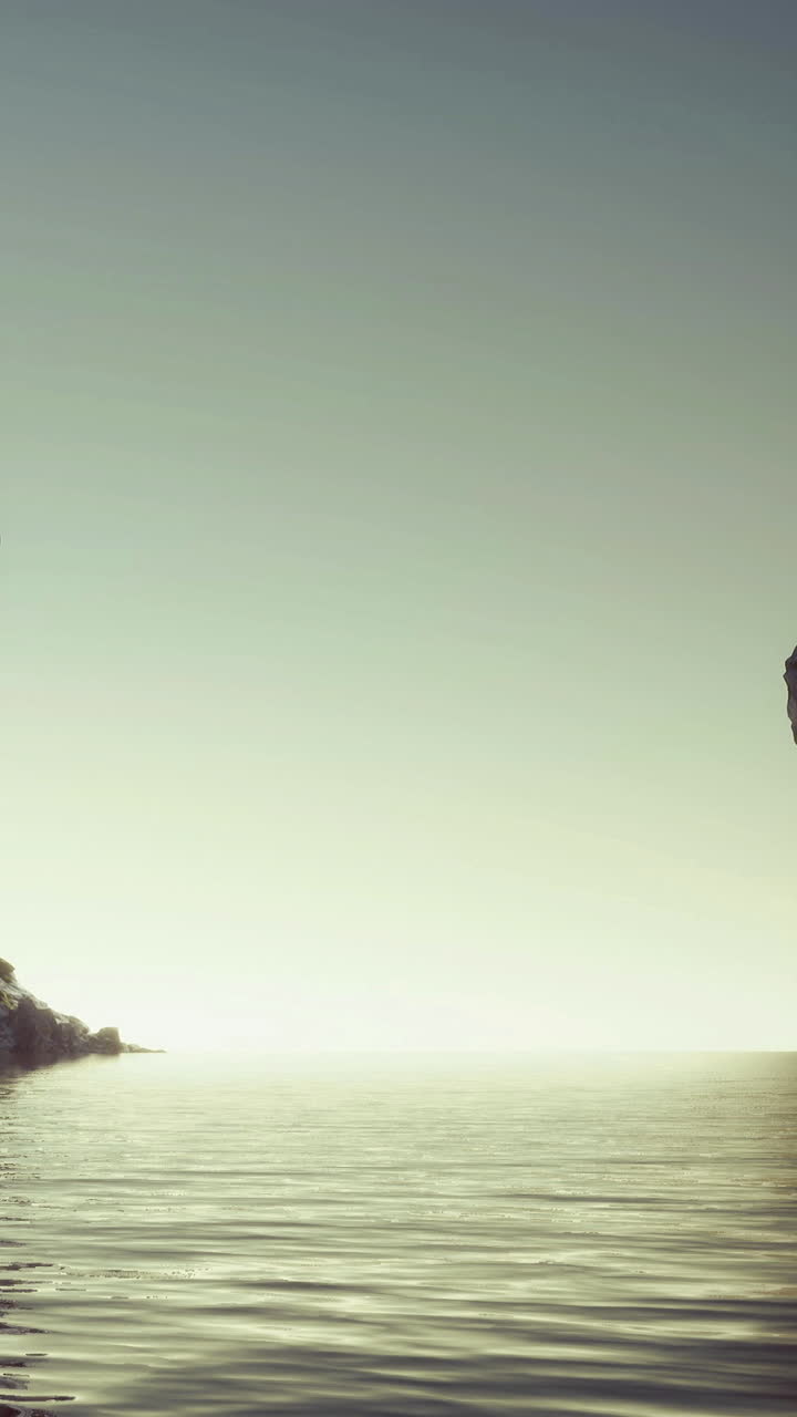 Sunrise over a quiet sea and rocky shore with gentle water reflections