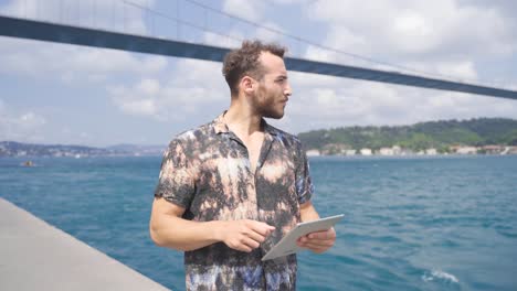 young man using tablet while walking. working by the sea.