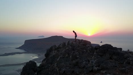 imágenes épicas de drones de un excursionista que llega al pico de una montaña al atardecer sobre la playa de balos en creta, grecia