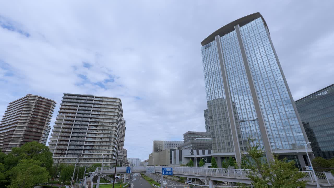 A low-angle shot of a Tokyo cityscape with a variety of modern glass skyscrapers and residential buildings against an overcast sky