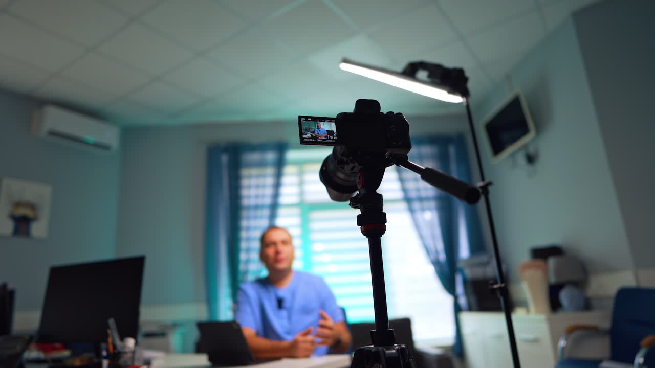 Modern camera on tripod recording a man talking at backdrop. Low angle view. Video blog creation. Selective focus