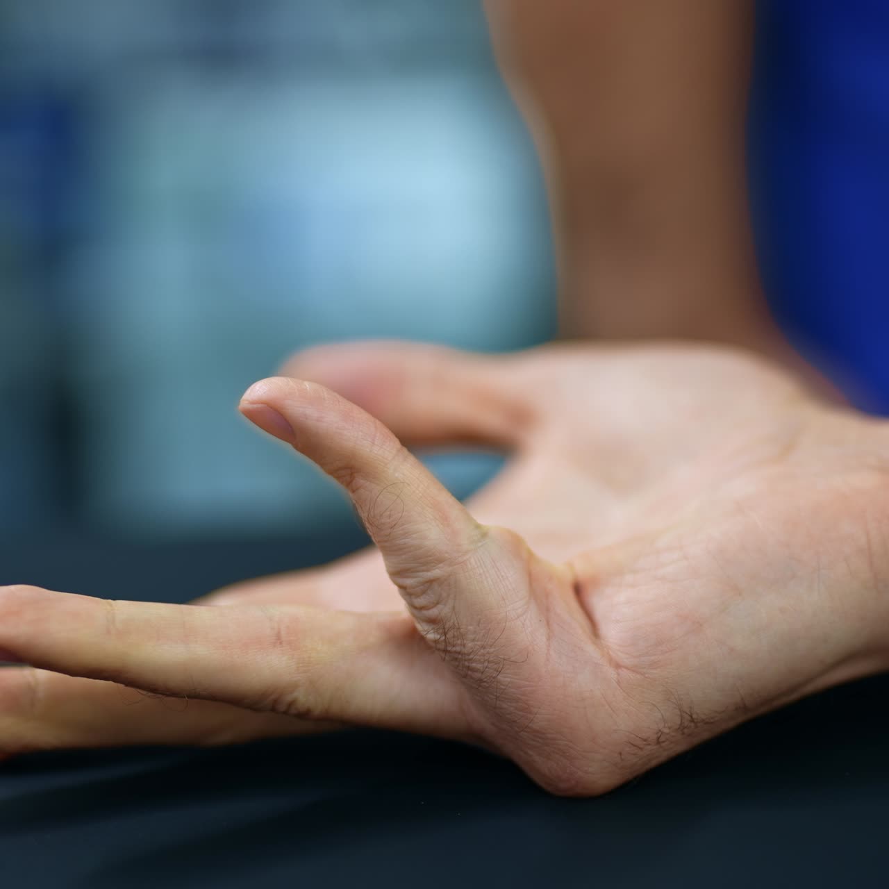 Hand of a male patient makes a fist and opens fist. Waiting for anesthesia work before staring a surgery. Doctor's silhouette at backdrop