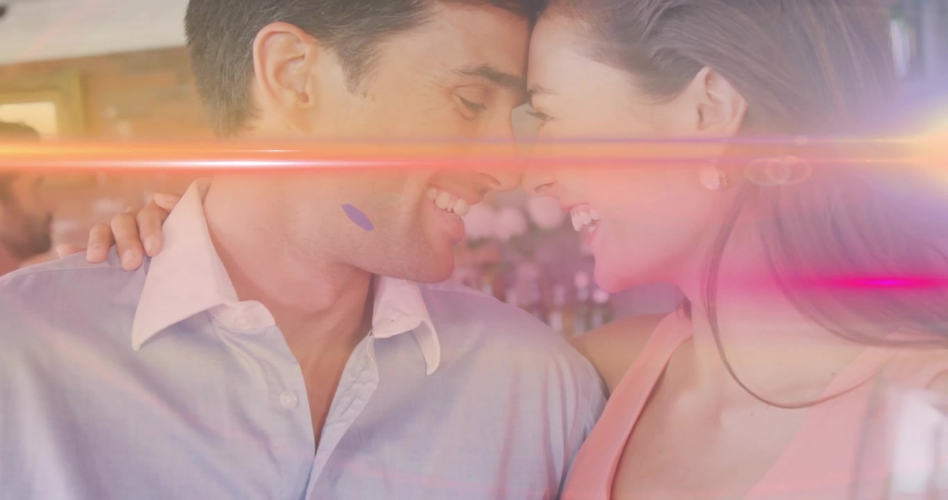 हॉस्पिटैलिटी में लेंस फ्लेयर के नीचे, बार में एक-दूसरे के माथे को छूता जोड़ा, एक-दूसरे को देखते हुए हंसी में बदल रहा है।
