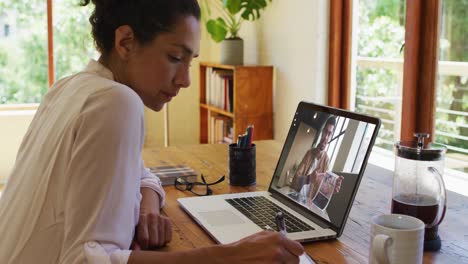 Mixed-race-businesswoman-sitting-at-desk-using-laptop-having-video-call-with-male-colleague