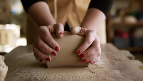 Close-up-footage-of-female-hands-with-beautiful-red-manicure-holding-clay-and-kneading-it-on-a-worktop.-Wearing-beige-apron.-Unrecognizable