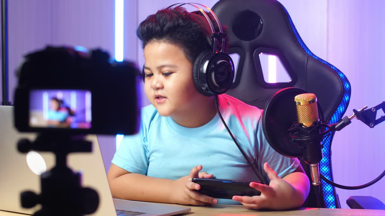 Asian Little Boy Holding Mobile Phone And Read Comment In Laptop Computer Then Talking To Camera While Live Stream