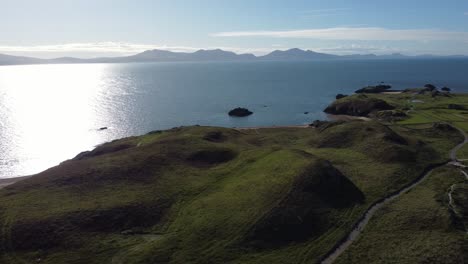 Aerial-view-Ynys-Llanddwyn-Welsh-island-hills-with-shimmering-ocean-and-misty-Snowdonia-mountain-range-across-the-sunrise-skyline