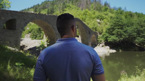 lone tourist looking around the view of the devils bridge and the river of arda, right at the foot of rhodope mountains in ardino, bulgaria