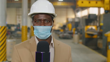 tv reporter in mask talking in mic in factory