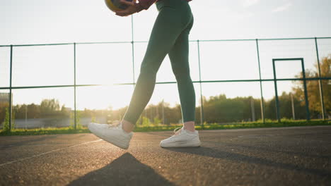 low angle view of athlete bouncing volleyball, stepping forward with sunlight creating a golden glow on the ground, preparing for a serve or play during volleyball practice