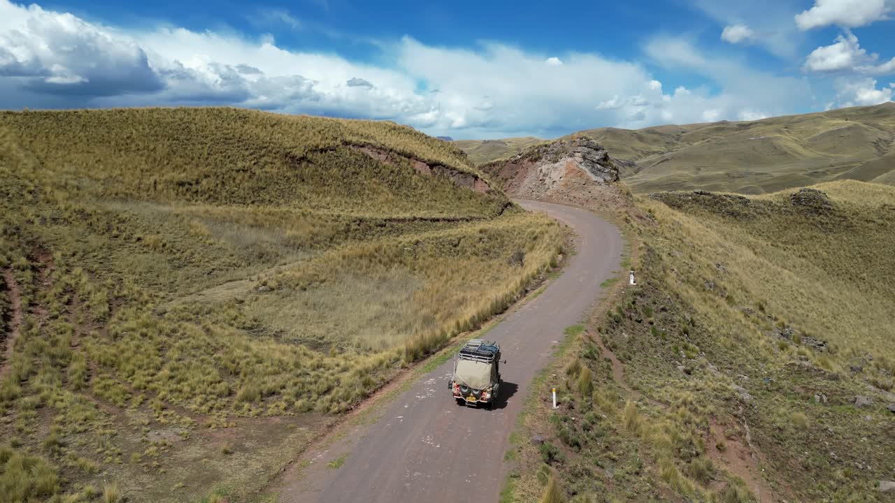 Cinematic drone shot of a tuk tuk driving through lush high-altitude meadows, the landscape glowing in afternoon sun