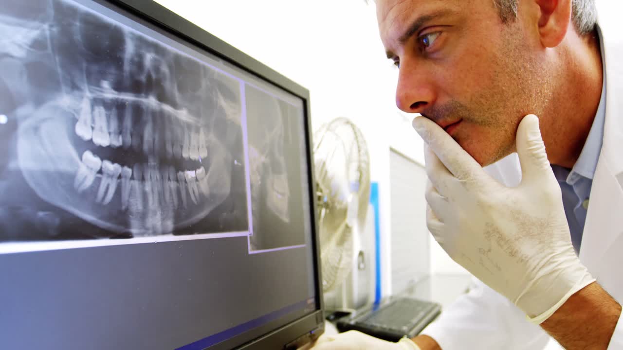 dentista pensativo examinando una radiografía en el monitor