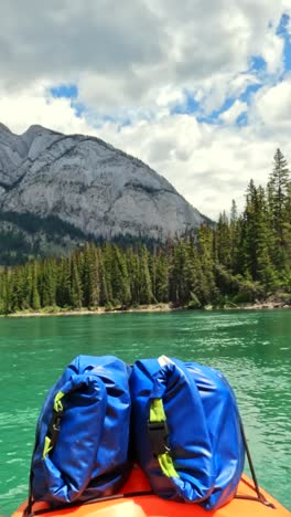 vertical pov captures a kayaker relaxing in their kayak as the bow river’s gentle currents carry them downstream at a slow pace. the calm flow of the water complements the stunning surroundings.