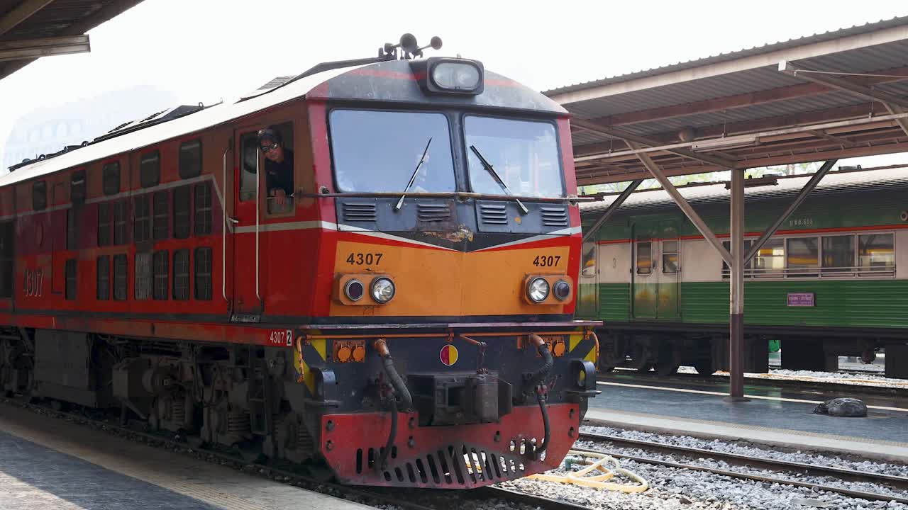 Locomotiva diesel rossa che si muove lentamente si avvicina alla piattaforma della stazione alla luce del giorno, vista statica laterale angolare della telecamera