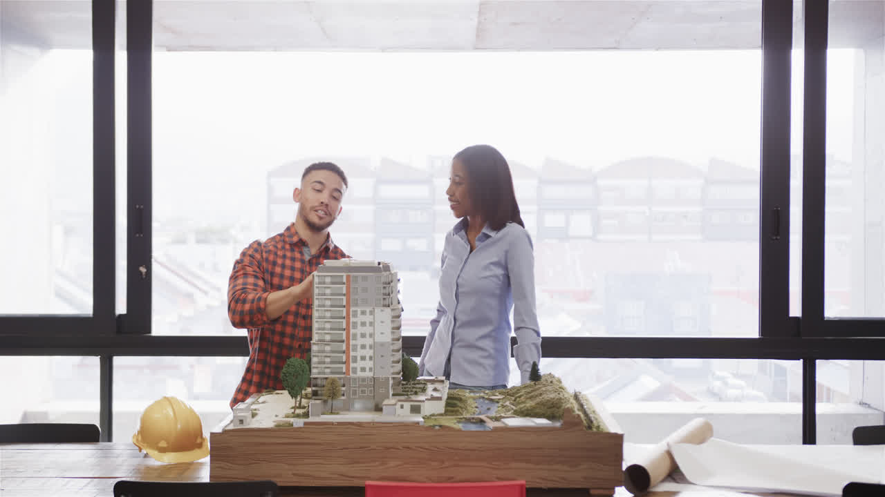 Diverse male and female architect discussing architectural model in office, slow motion