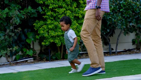 Vista-Lateral-Del-Joven-Padre-Negro-Y-Su-Pequeño-Hijo-Jugando-En-El-Patio-Trasero-De-Su-Casa-4k