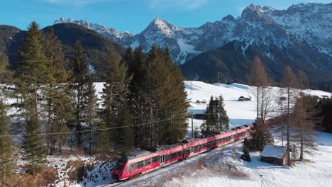 aerial: train near mittenwald emerging among trees and with the karwendel mountains in the blackground in a sunny day