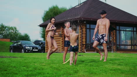 family in the backyard of a country house in the summer relax playing with water and hosing