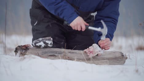 man hammering fish head and meat on wood during snowfall at winter