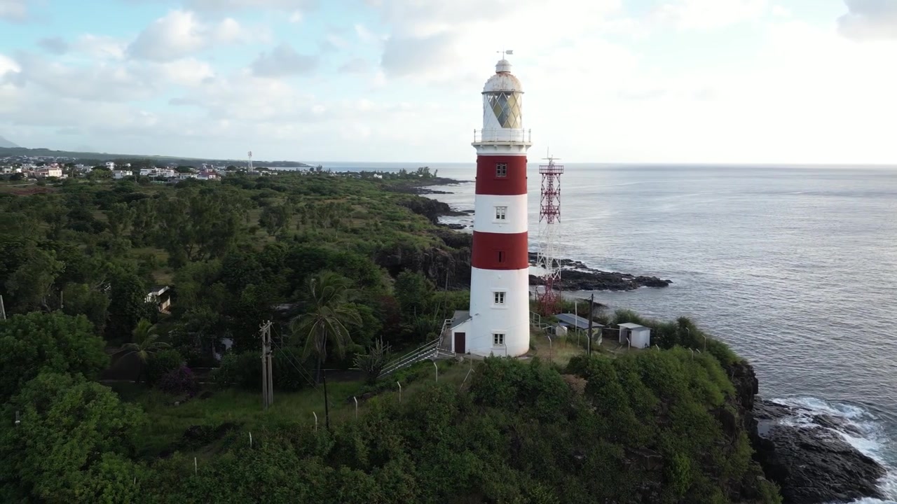 Prospettiva aerea con drone dell'iconico faro Albion rosso e bianco che si erge su una scogliera rocciosa a picco sulla costa di Mauritius. Punto di riferimento storico per la navigazione marittima al tramonto.