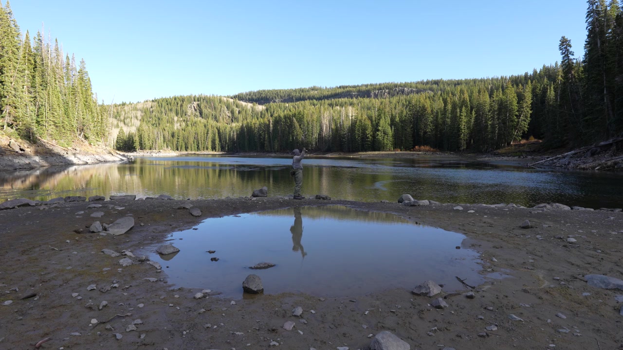 Stille vidvinkeloptagelse fra jorden af en enlig fisker, der kaster ud ved en stille alpesø på Colorados Grand Mesa, fisker efter regnbueørred og bækørred i Rocky Mountains
