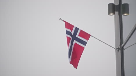 the norwegian flag, moved by the wind and attached to the big supermarket in the city center of longyearbyen flaps in the wind during a storm in a moddy grey weather