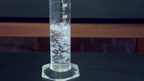 close up of clear liquid being poured into a 1000ml graduated cylinder on a black lab bench in a high school chimistry classroom