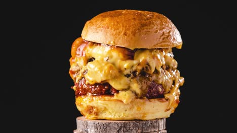 big pulled pork and beef burger with many cheese and bbq sauce rotating con dark background
