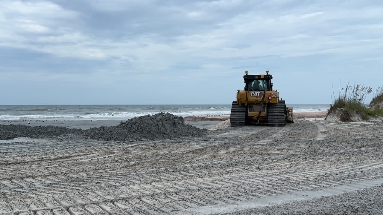 Tracked CAT bulldozer driving by on beach, sand replenishment
