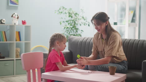 happy woman gives green seedling to little daughter at home