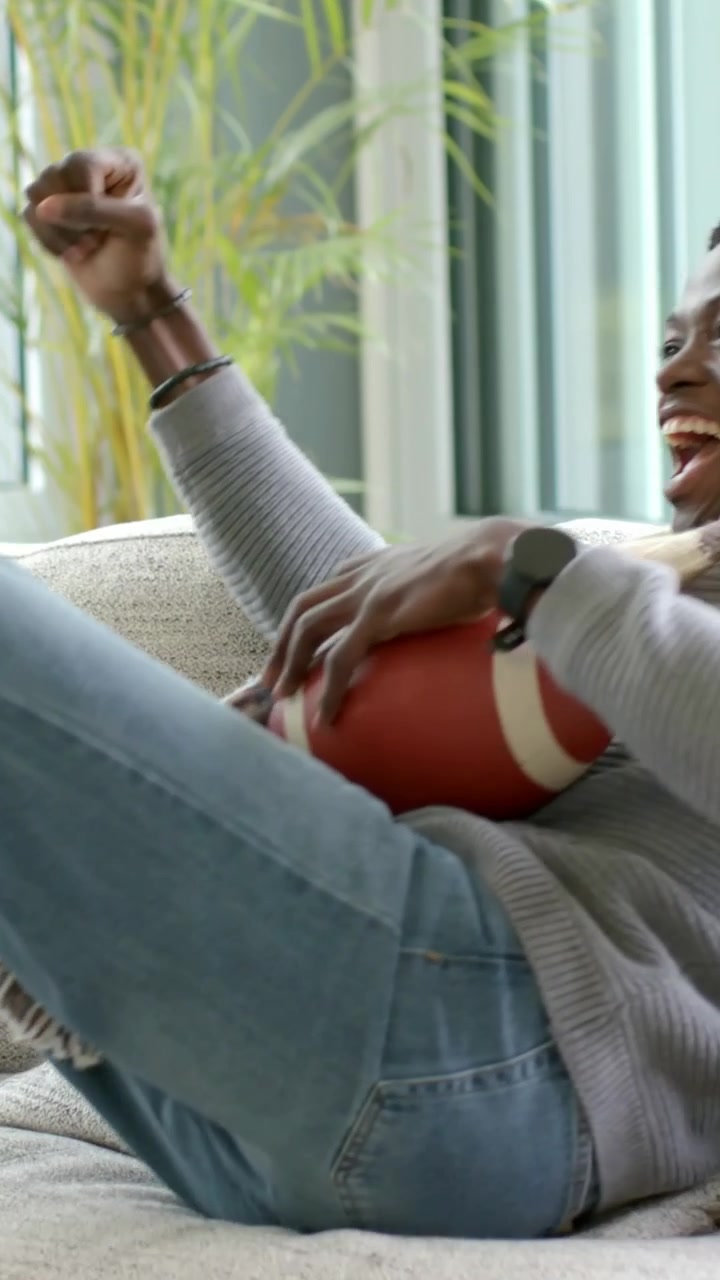 Vertical video: Holding man with scarf grabbing ball shifting on sofa at start, reacting off-screen