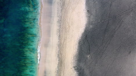 Aerial-shot-of-an-empty-sandy-beach-with-gentle-waves-hitting-the-coastline