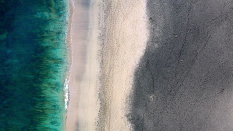 aerial shot of an empty sandy beach with gentle waves hitting the coastline