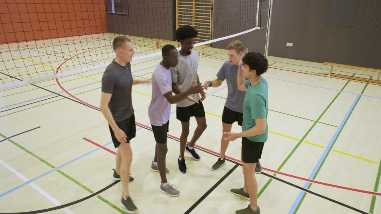 Male team lining opposite net in gym with server tossing volleyball playing rally cheering point