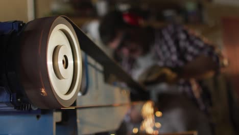 Close-up-of-caucasian-male-knife-maker-in-workshop-using-sander