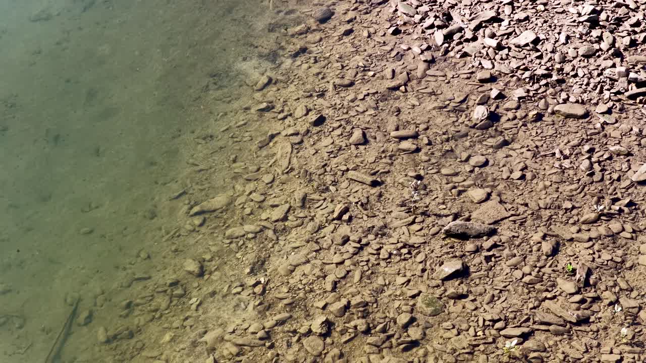 Aerial footage of a rocky shoreline with clear water, captured in natural daylight, showcasing serene and tranquil scenery