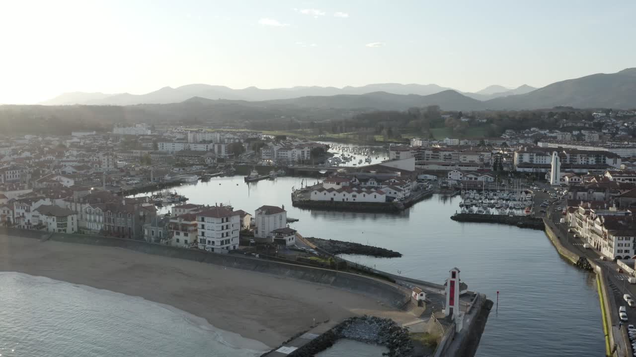 Picturesque Saint-Jean-de-Luz harbor, lighthouse, beach, Pyrenees mountains in background, France. Aerial drone