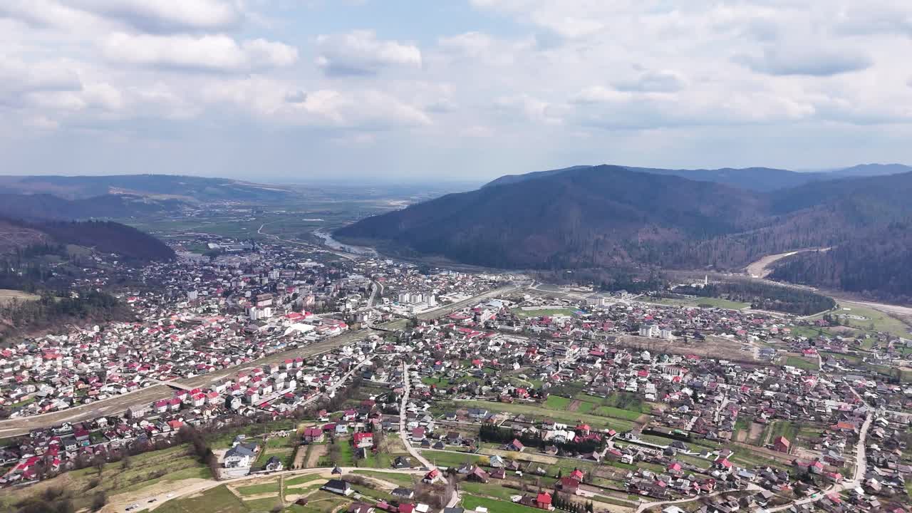 Panoramiczny widok z drona na Gura Humorului w Rumunii, ukazujący rozległy układ miasta, dolinę rzeki i otaczające Karpaty pod częściowo zachmurzonym niebem