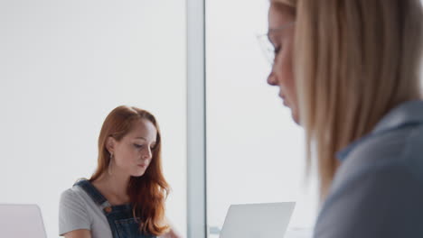 Pull-Focus-Shot-Of-Two-Casually-Dressed-Young-Businesswomen-Working-On-Laptops-And-In-Office