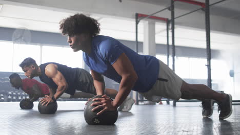 men doing push-ups on medicine balls during intense gym workout session
