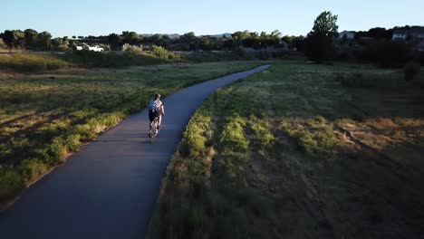 Drohnenaufnahme,-Die-Einem-Radfahrer-Folgt,-Der-Für-Einen-Triathlon-Trainiert,-Indem-Er-Mit-Seinem-Fahrrad-Einen-Schmalen-Radweg-Hinunterfährt