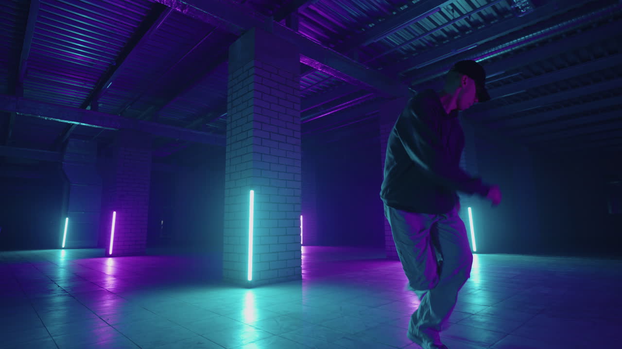 A steel man dances hip-hop freestyle in a modern style in a hall with neon light in purple blue colors. Male Professional Hip Hop Dancer