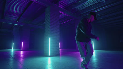 a steel man dances hip-hop freestyle in a modern style in a hall with neon light in purple blue colors. male professional hip hop dancer
